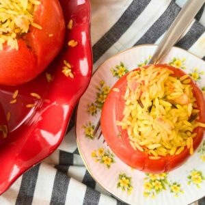 There is a rice stuffed tomato on a yellow floral plate. There are more tomatoes off to the side.