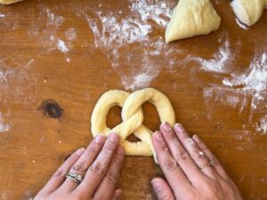 A woman shaping dough into a pretzel shape, on a wooden table.