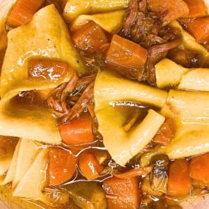 A close up view at a bowl of beef stew with large noodles in it.