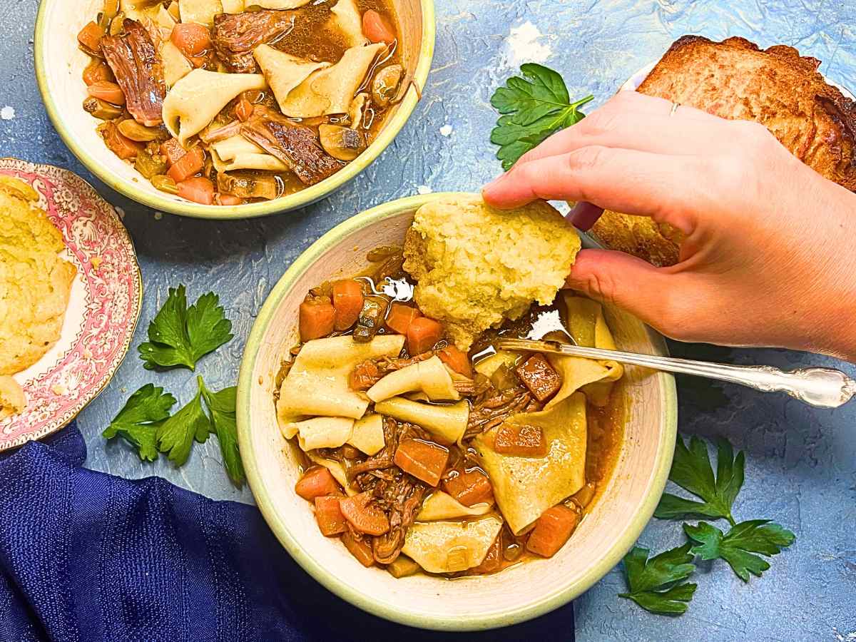 A woman dipping a biscuit into a bowl of beef stew.