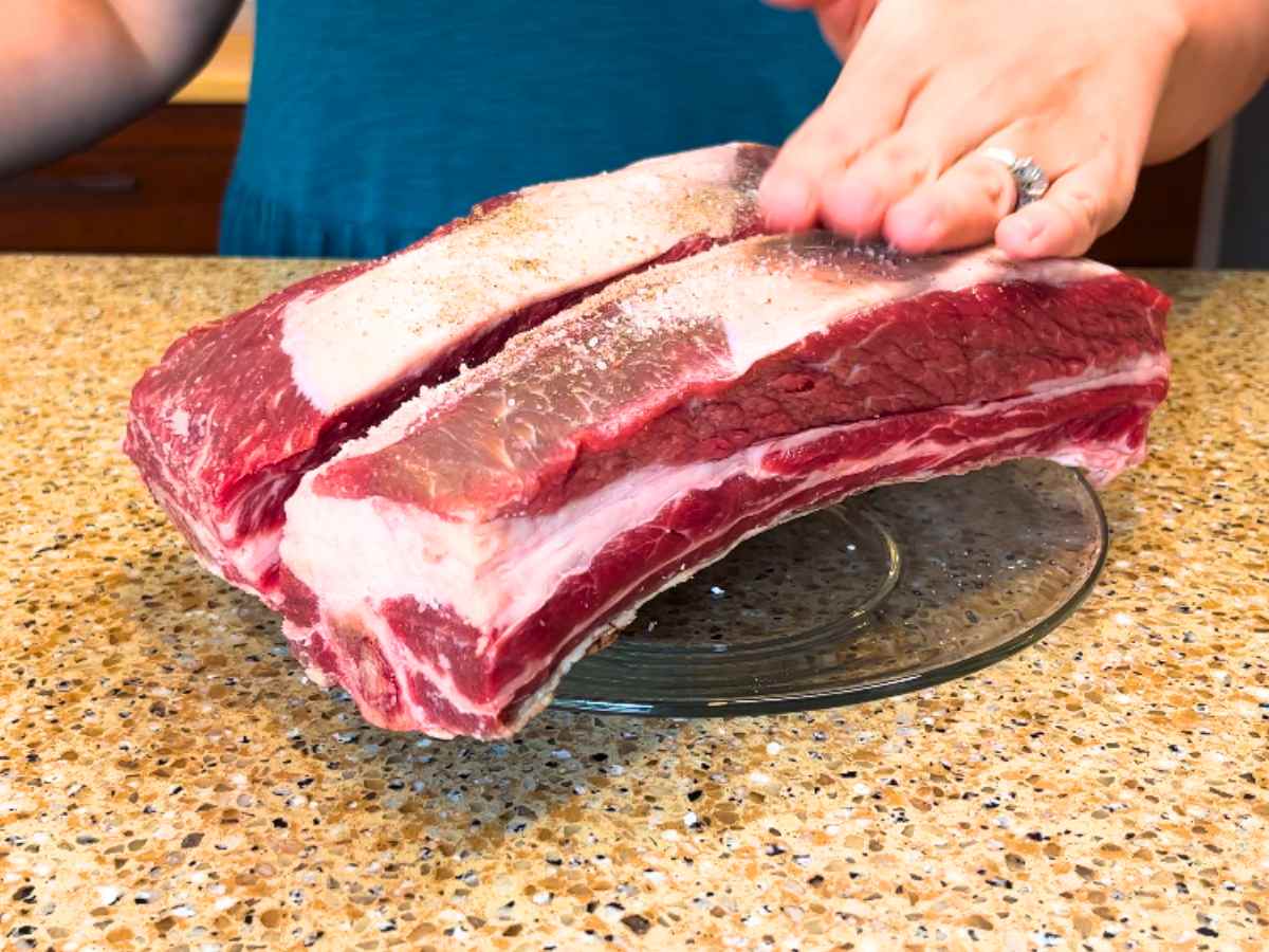 A woman pressing salt and pepper into a beef short rib.