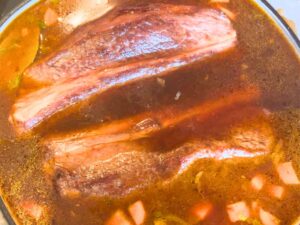 Beef short ribs simmering in a mixture with beef stock and vegetables.