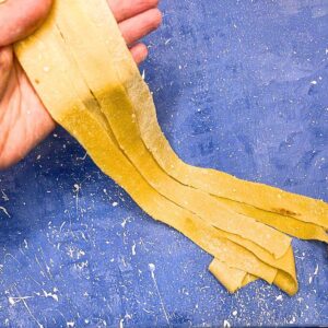 A woman holding fresh pasta noodles on a blue table.