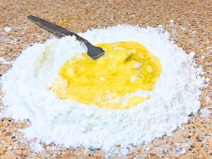 A pile of flour with a yellow egg mixture in the centre.