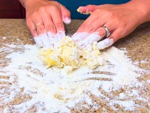 A woman mixing pasta dough with her hands.