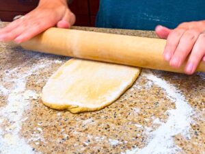 A woman rolling out pasta dough with a rolling pin.