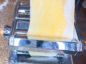 A woman rolling a sheet of pasta through a pasta roller.