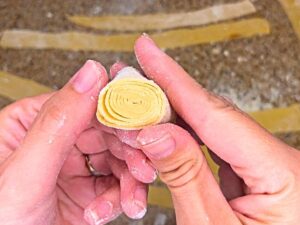 A woman holding a spiral of cut pasta dough.