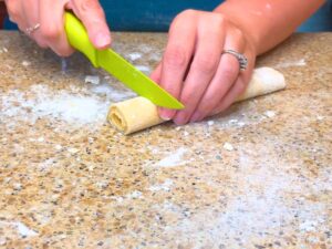 A woman cutting a spiral log of pasta dough into sections.