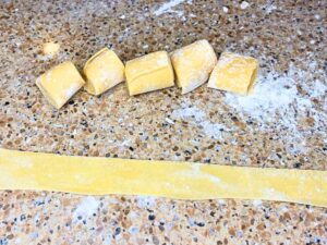 A long strip of a fresh pasta noodle. There are more in the background that are unrolled.