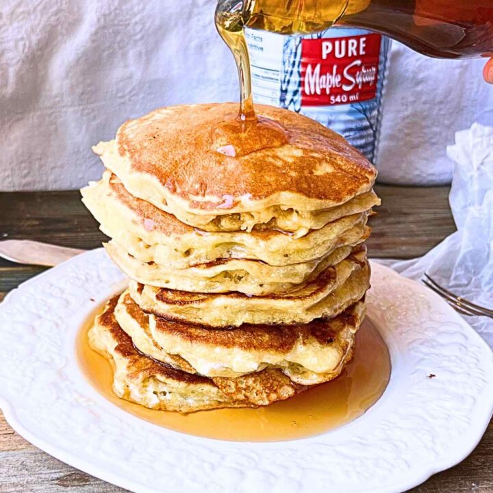 A woman pouring maple syrup onto a stack of pancakes.