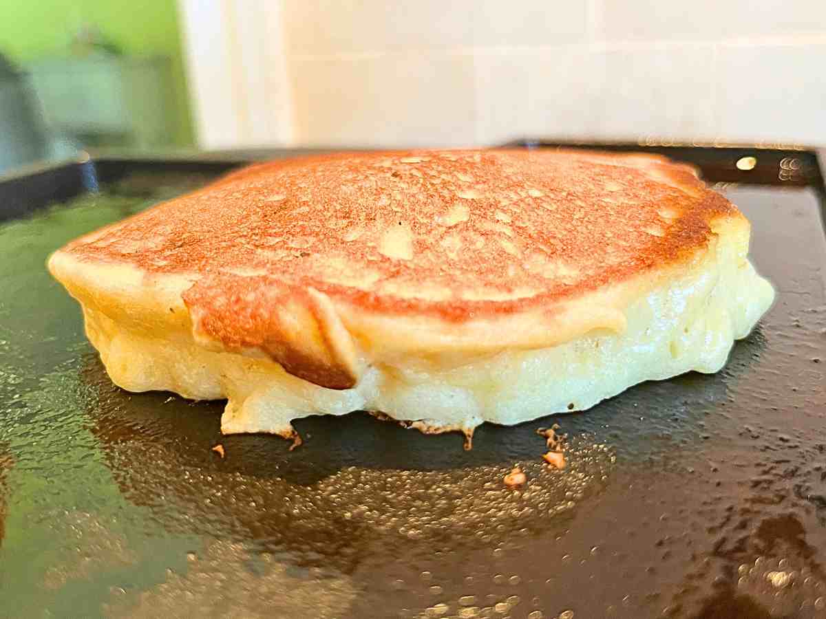 A pancake cooking the second side on a griddle.