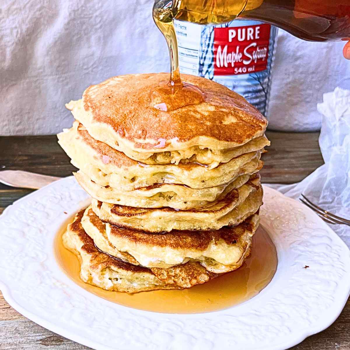 A woman pouring maple syrup onto a stack of pancakes.