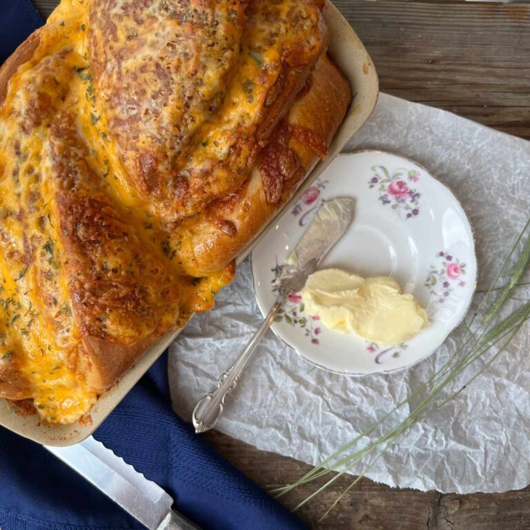 A over top look at a loaf of cheese bread. There is a pink floral plate beside with butter and a butter knife.