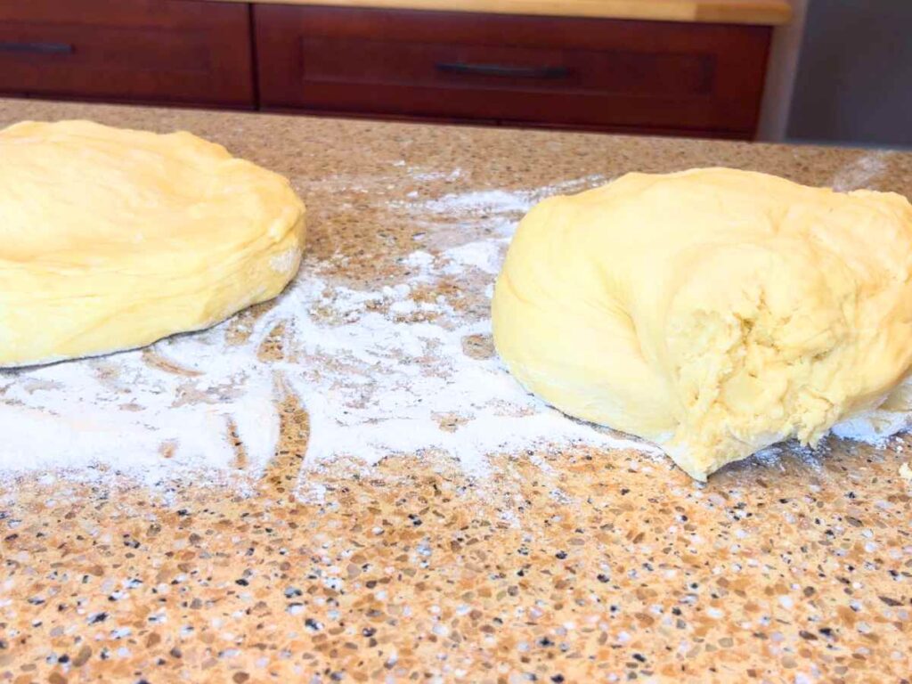 Two balls of bread dough on a counter with flour.