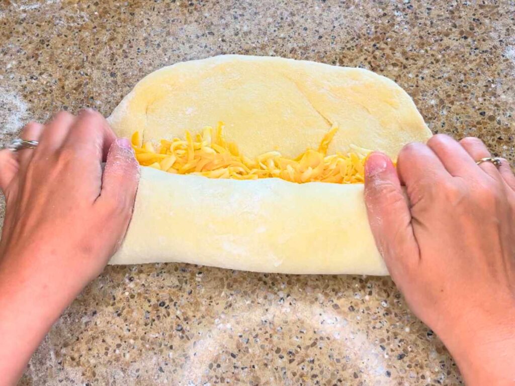 A woman rolling up bread dough with grated cheese inside.