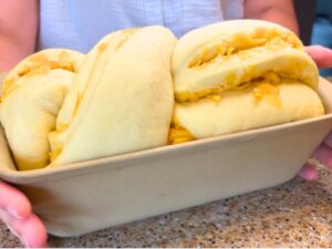 A twisted loaf of cheese bread is risen inside of a loaf pan.