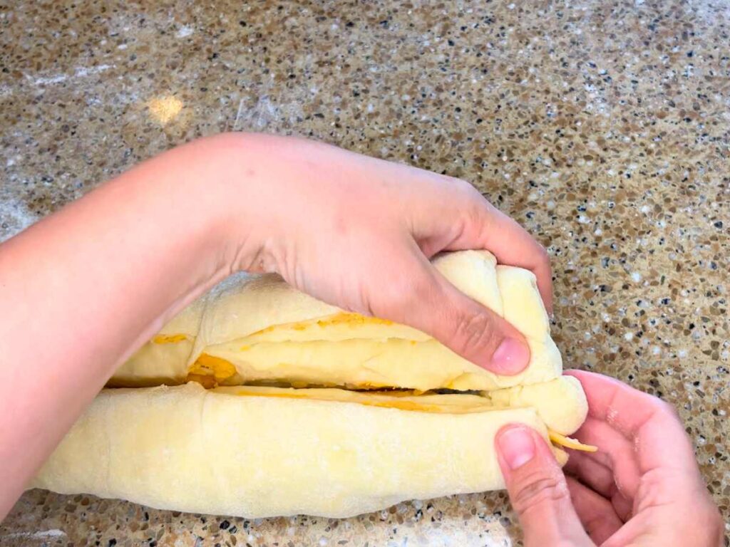 A log of dough with cheese inside has been cut in half lengthwise.