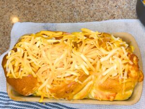 A partially baked loaf of cheese bread has grated cheese sprinkled on top.