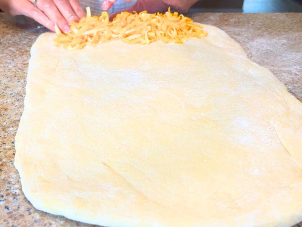 A woman placing grated cheese on a large rectangle of dough.