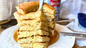 There is a stack of pancakes on a white plate. There is a forkful in front showing the inside of the pancakes.