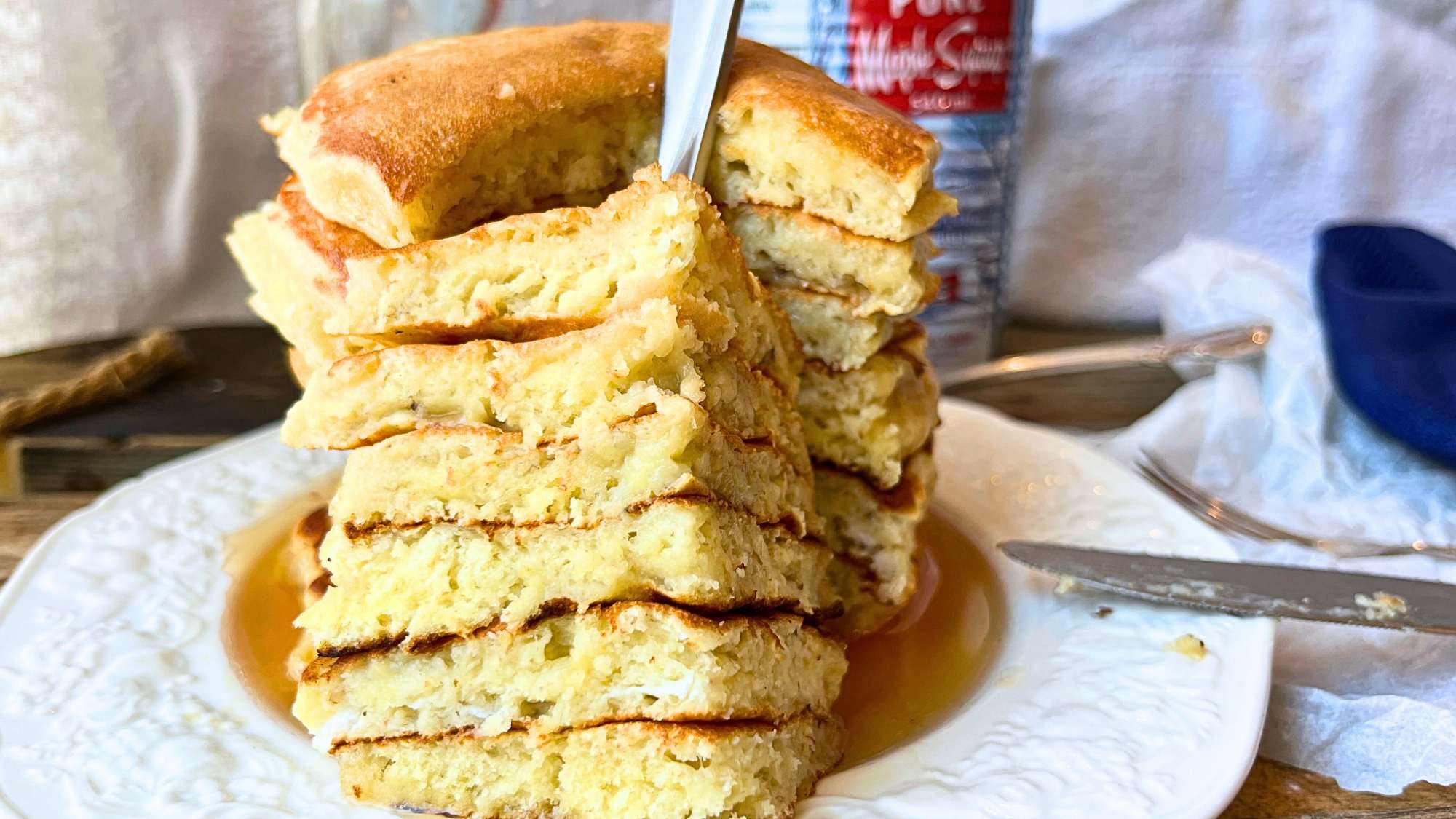 There is a stack of pancakes on a white plate. There is a forkful in front showing the inside of the pancakes.