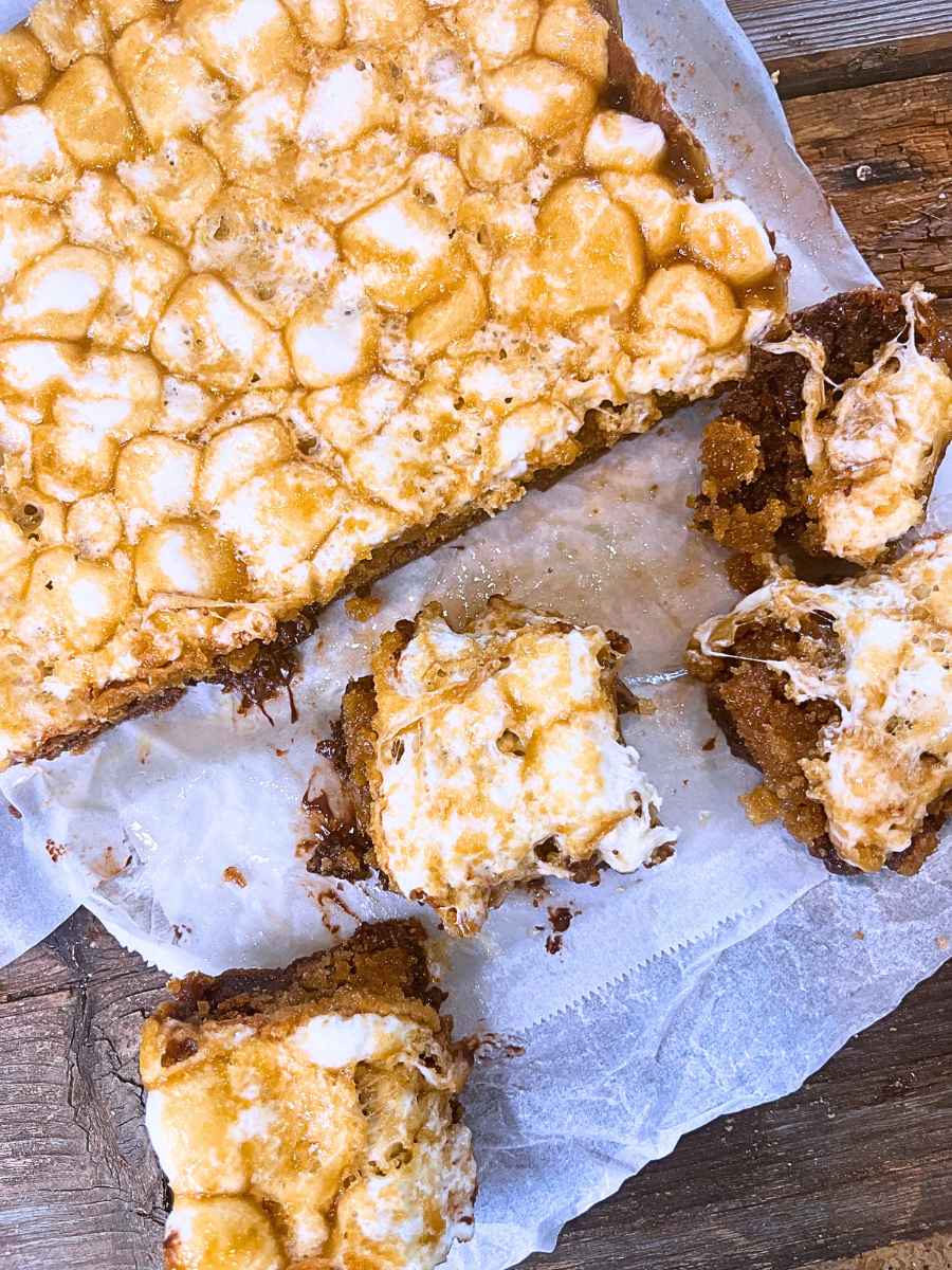 Marshmallow caramel dessert squares being cut on a piece of parchment paper.