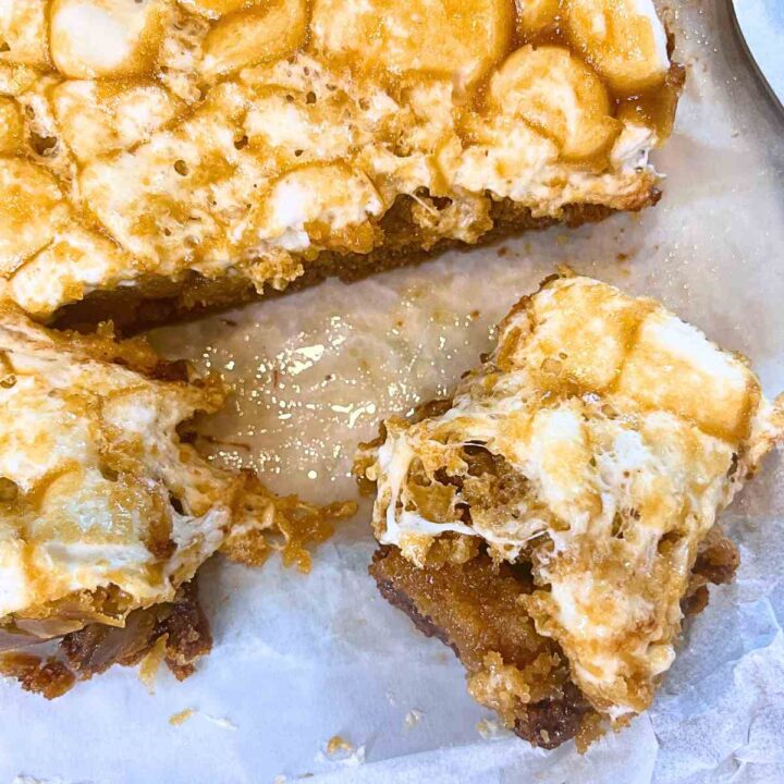 Marshmallow and caramel squares being cut on a piece of parchment paper.