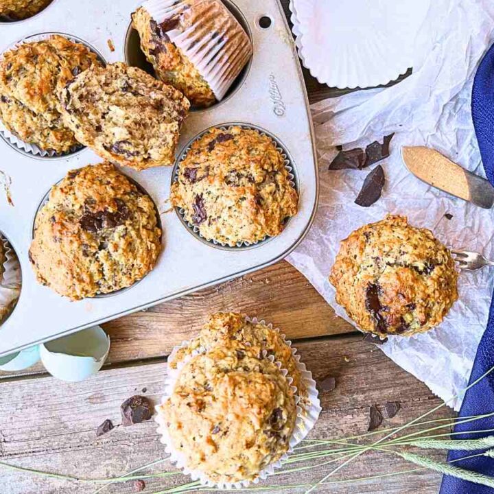 An overhead view of some oatmeal banana chocolate chunk muffins. Some are still in the muffin tin. Two are stacked and one is off to the side.