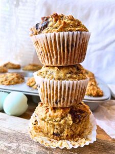 Three stacked banana chocolate chunk muffins. There are more muffins in the background.