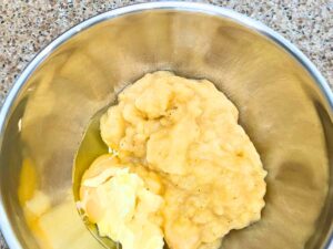 A large metal bowl with mashed bananas, egg, and butter inside.