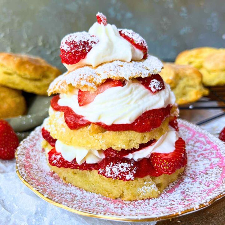 A strawberry shortcake on a pink tea plate. There are more biscuits in the background.