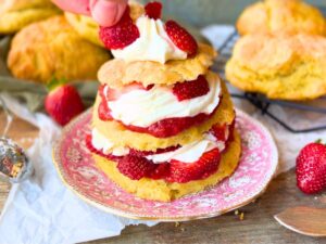 A woman placing a piece of strawberry on top of a strawberry shortcake.