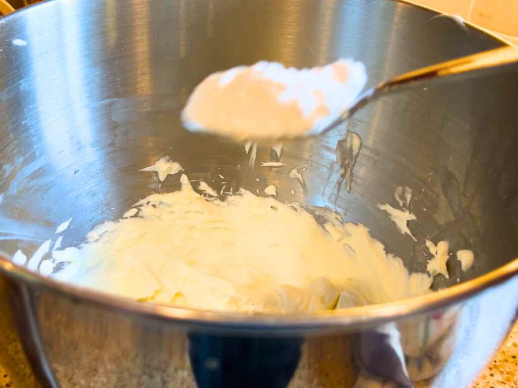 A woman adding icing sugar to whipped cream.