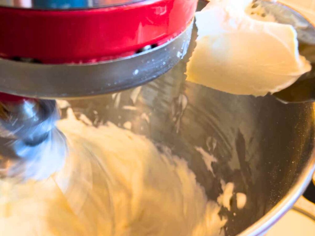 A woman adding cream cheese to whipped cream.