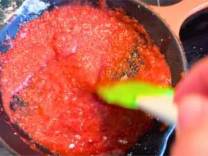 Woman stirring strawberry sauce in a pan on the stove top.