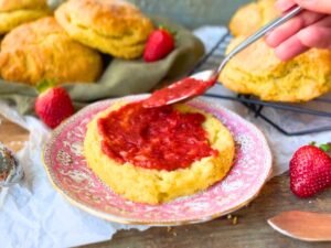 A woman spreading strawberry sauce onto a biscuit.