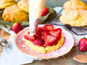 A woman using a piping bag to put whipped cream onto a strawberry shortcake.