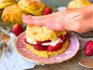 A woman putting a biscuit top of top of a strawberry shortcake.