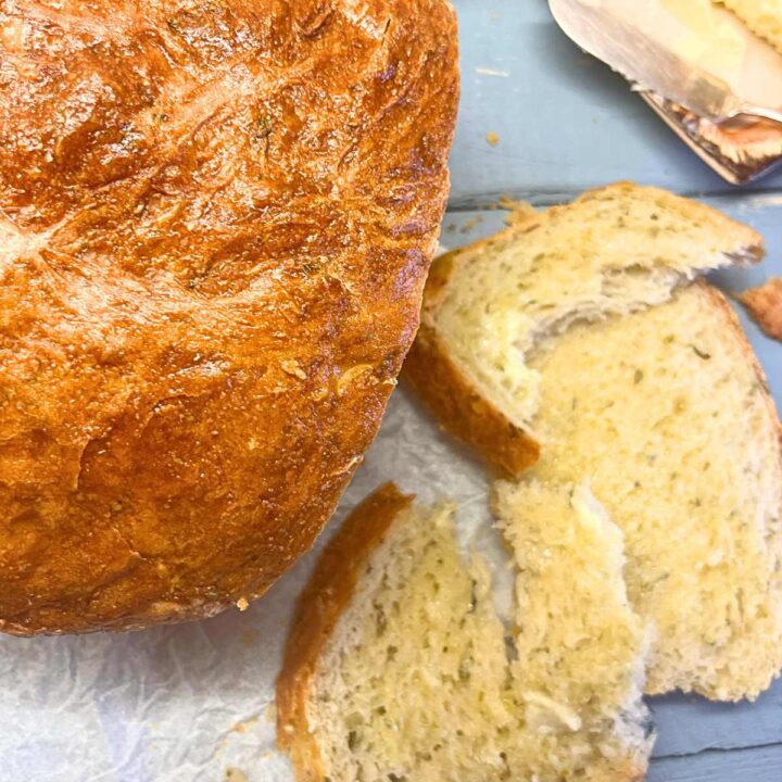 There is an overhead look at a loaf of bread. There are some slices in front with butter spread on them.