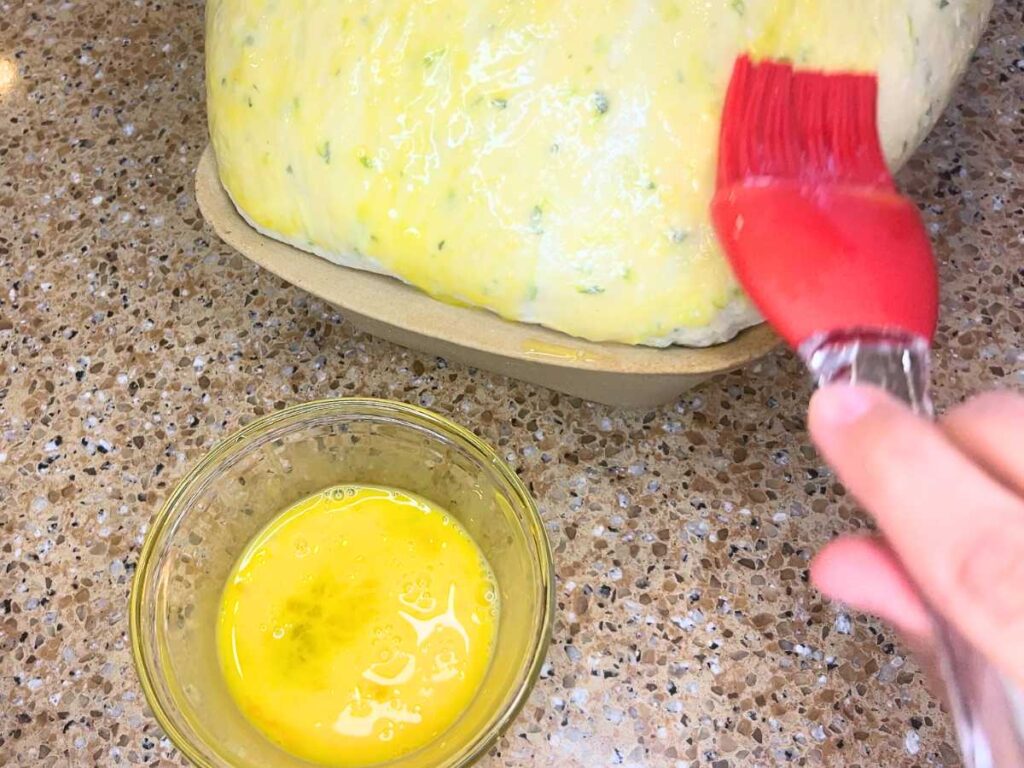 A woman brushing the top of some bread dough with egg wash.