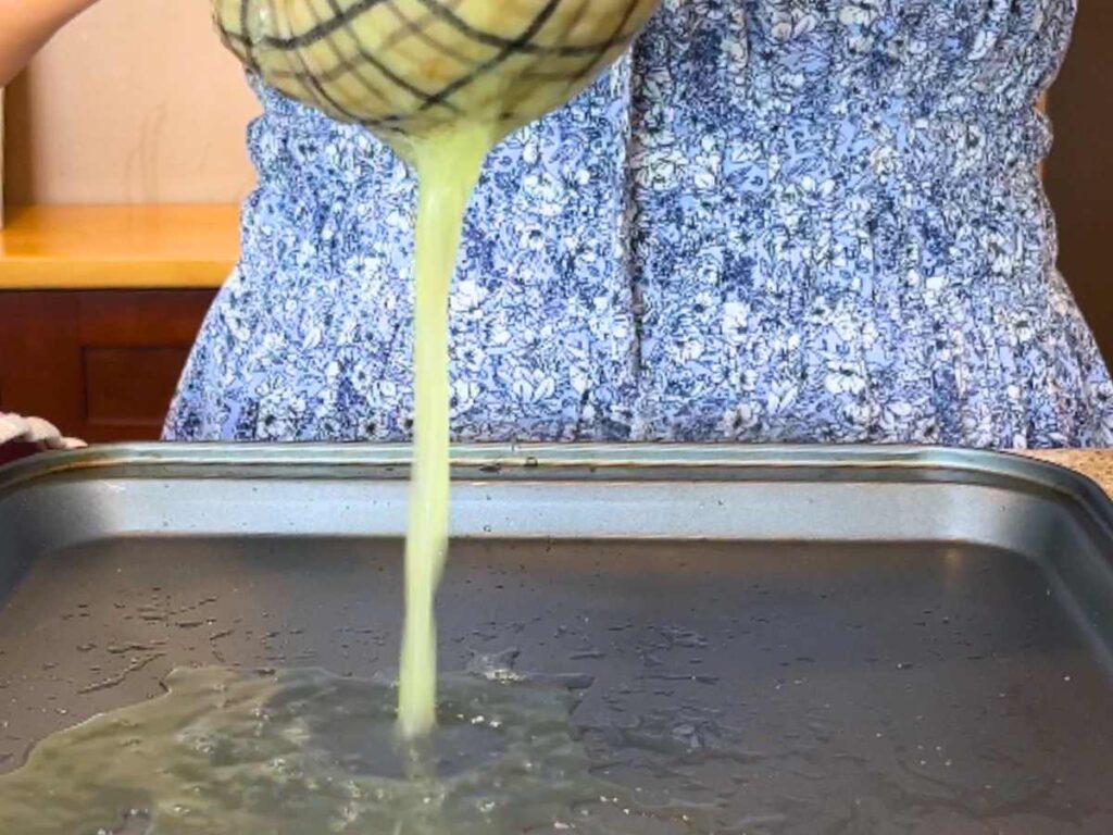 A woman squeezing liquid from zucchini through a kitchen towel.