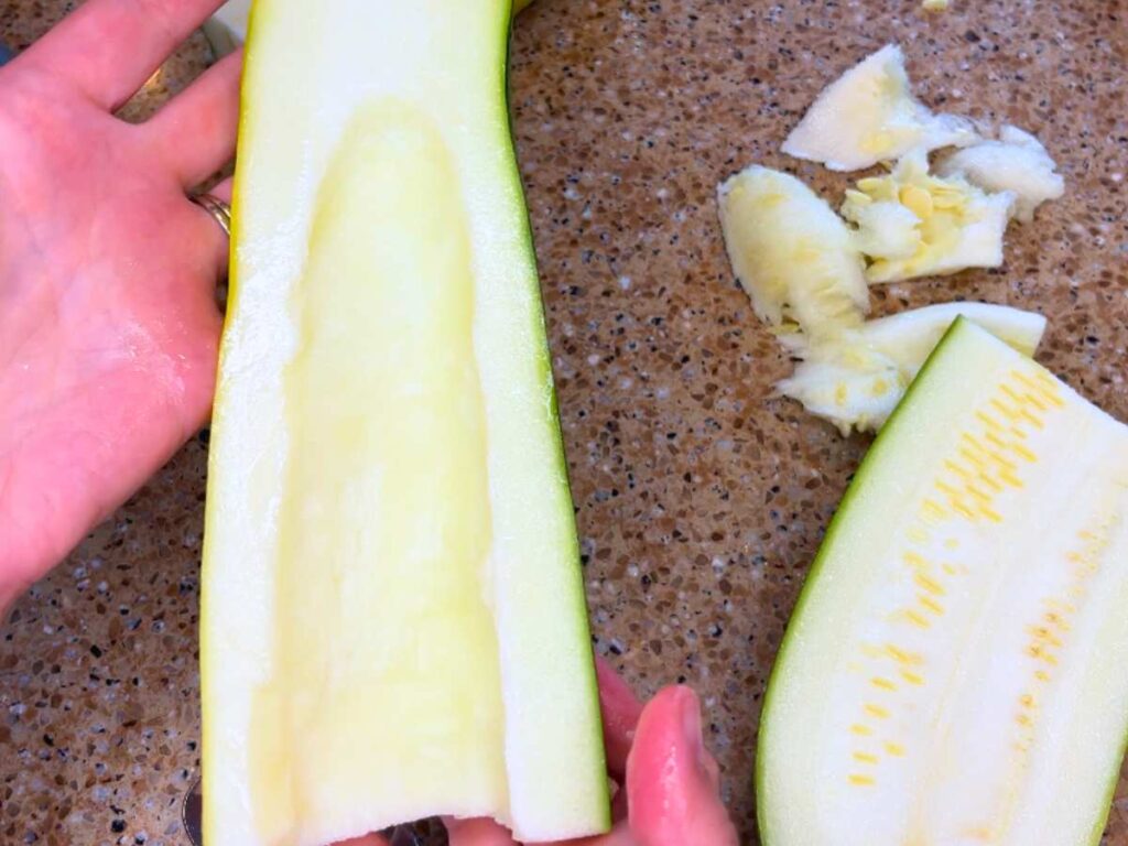 A woman holding a zucchini that is cut in half and the seeds are scooped out.