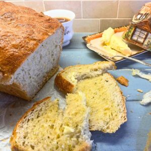 A bread loaf with some slices in front. There is a butter dish in the background.