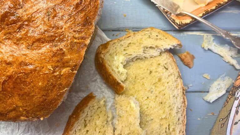 A loaf of bread with zucchini backed in it. There are slices of bread in front of the loaf with butter spread on top.