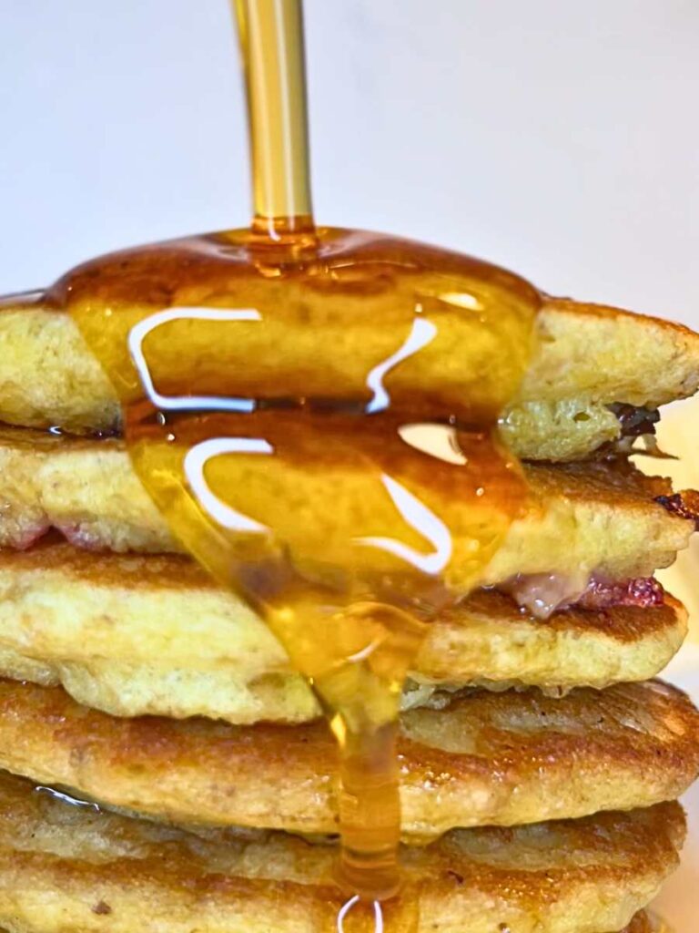 There is a woman pouring maple syrup onto a stack of pancakes.