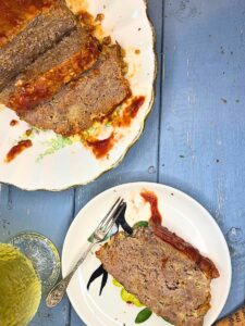 An over head view of a sliced meatloaf on a platter. There is one slice in front with a fork.