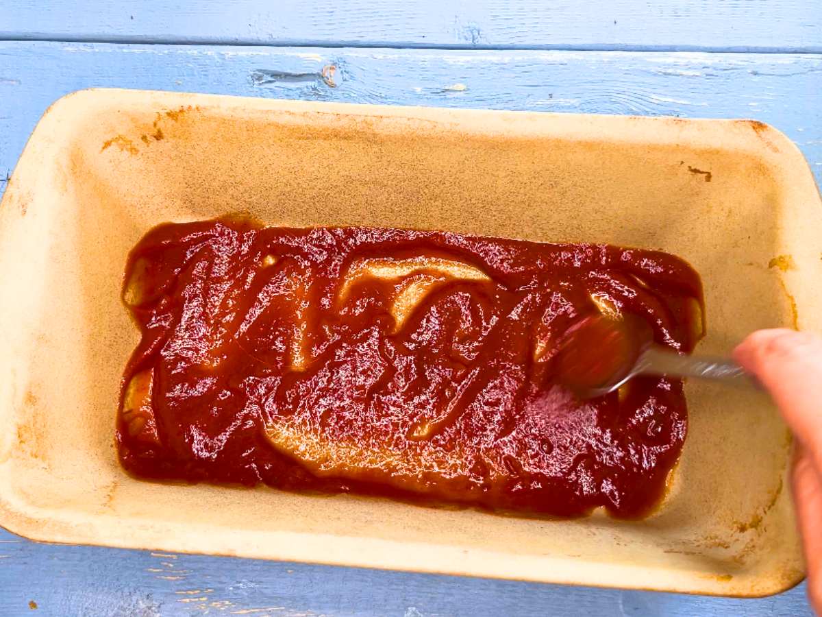 A woman spreading chili sauce into the bottom of a loaf pan.