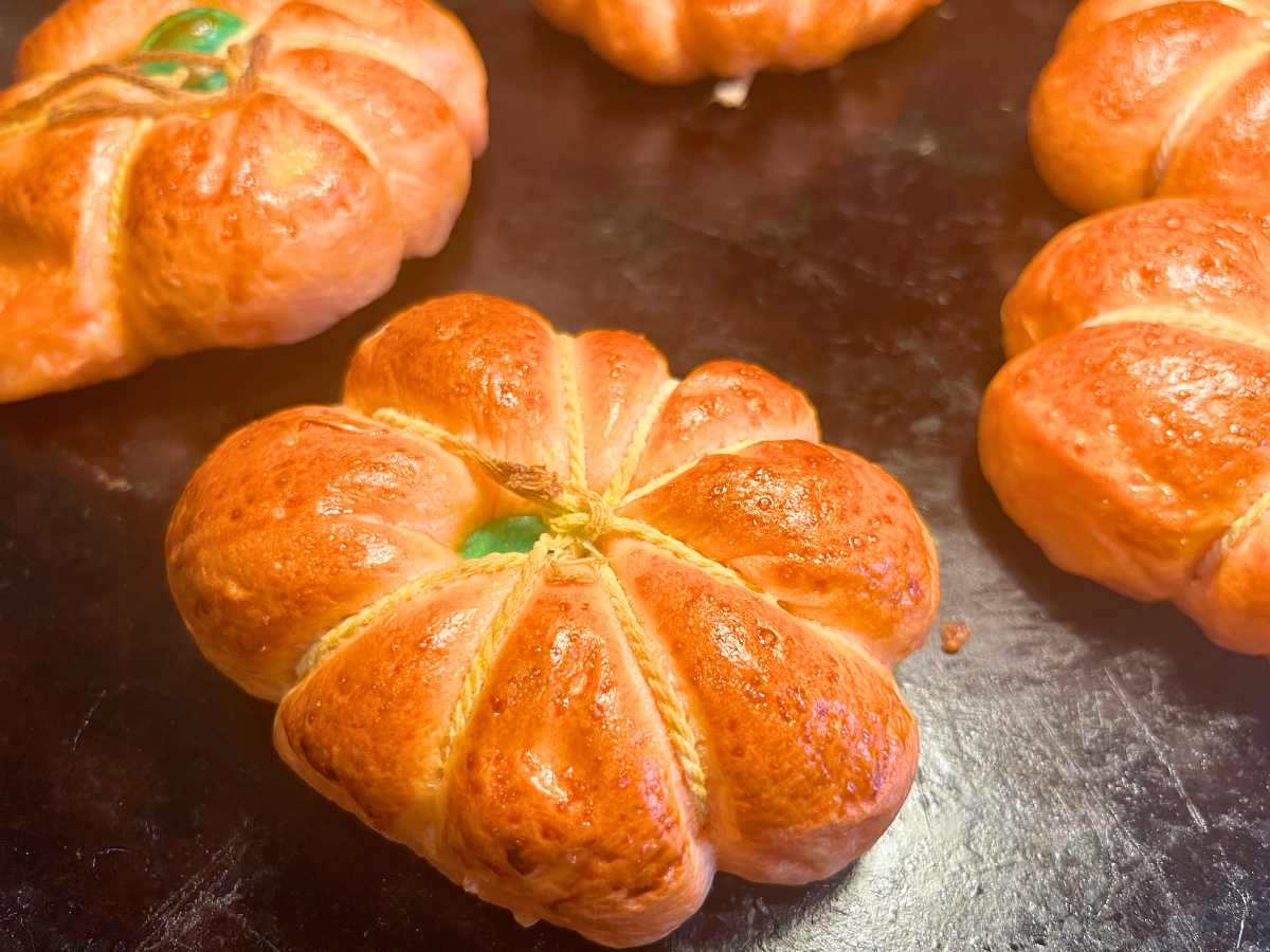 Some baked pumpkin shaped bagels on a pizza stone.