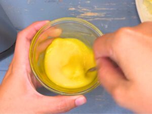 A woman is beating an egg in a small glass bowl.